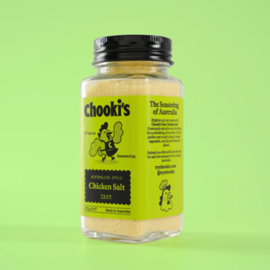 A bottle of Chooki's Australian Style Chicken Salt Zest on a solid light green background. The product is in a clear glass bottle showing the pale yellow salt inside, with a black screw cap and a bright lime green label featuring the brand name and cartoon chicken illustrations.